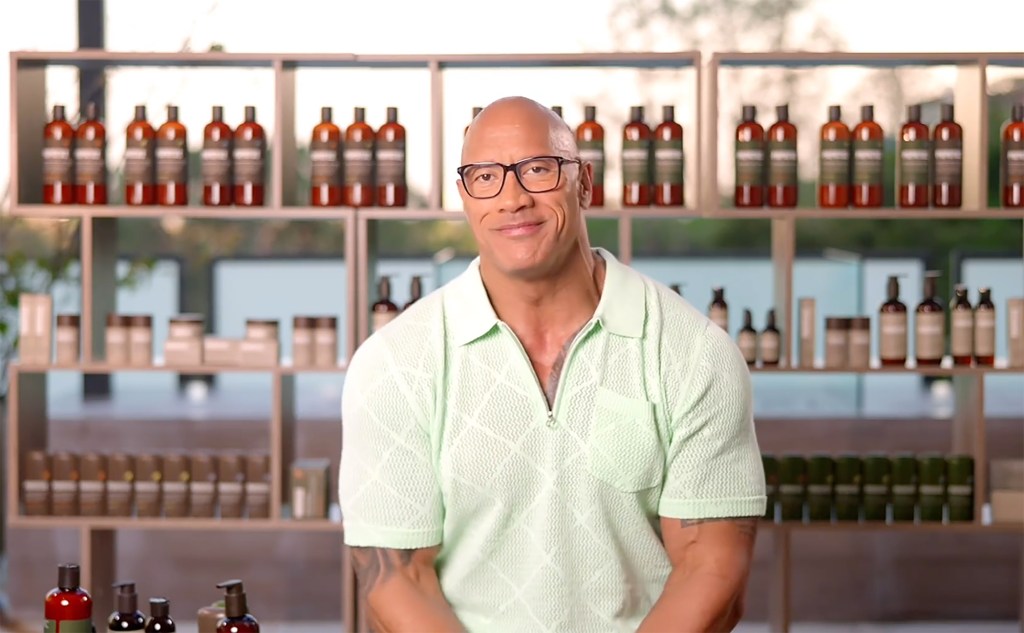 Dwayne Johnson with glasses sitting in front of men's care products