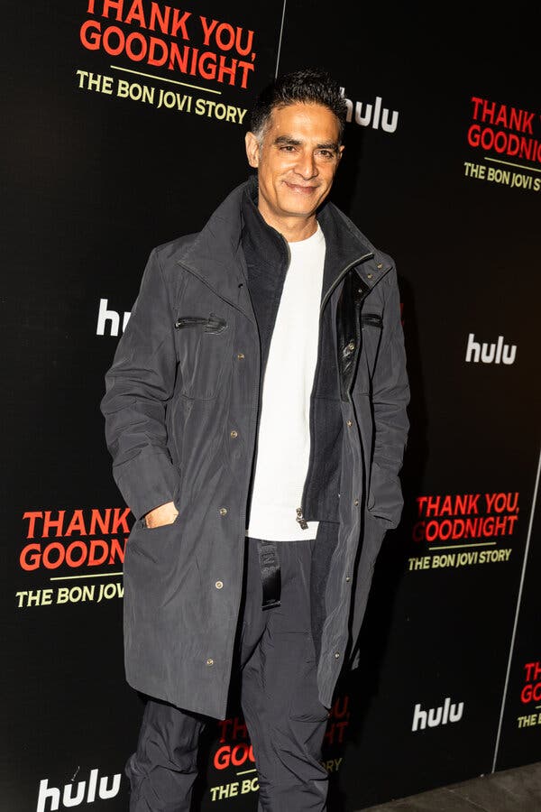 Gotham Chopra, wearing a gray jacket over a white T-shirt and gray pants, poses on the red carpet for "Thank You, Goodnight."