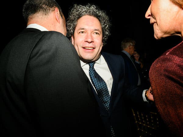 Gustavo Dudamel in a blue suit and tie, embracing people during a party.