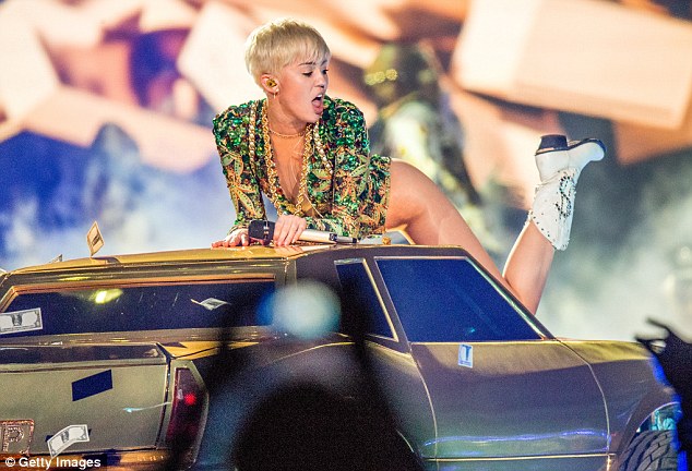 Don't mind me: Miley sprawls across the car as dollar bills rain down