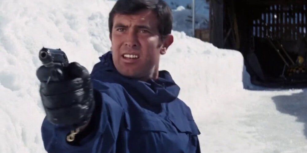 George Lazenby as James Bond pointing a gun in the snow in On Her Majesty's Secret Service