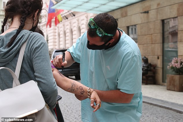 Fans: The star kept things casual in an over-sized blue T-shirt and grey shorts as he signed one lucky fan's arm outside his hotel