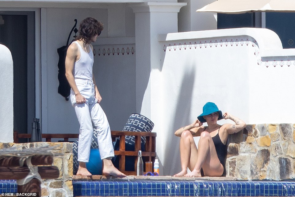 Casual: Miley lounged in her black bathing suit by the edge of the patio with her hat on