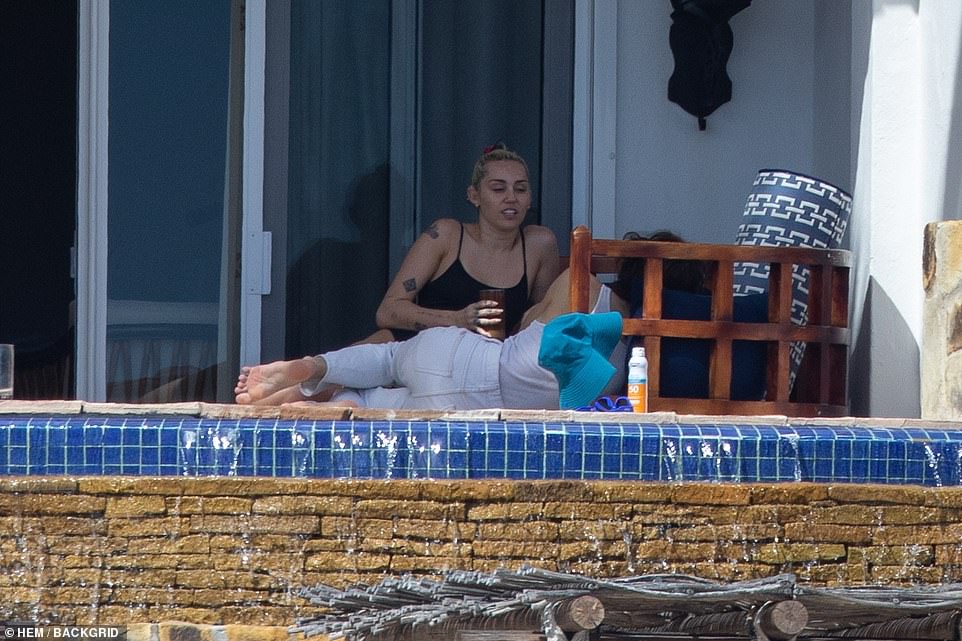 Close: The musician wore white jeans and a T-shirt tucked in, adding sunglasses with his hair tousled and loose around him; he lounged on the ground next to the star as she she sipped her beverage