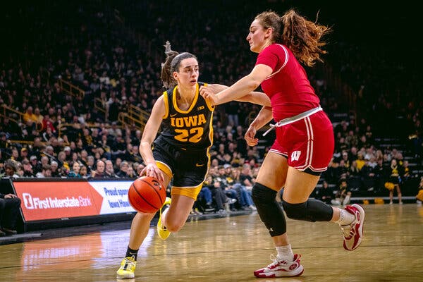 Caitlin Clark dribbles and a Wisconsin player defends at a basketball game in a packed stadium.