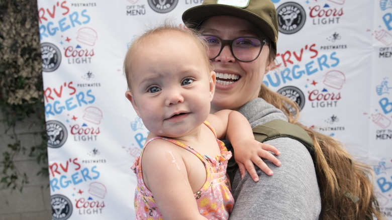 Ronda Rousey holds her daughter and poses for cameras outside a media event.