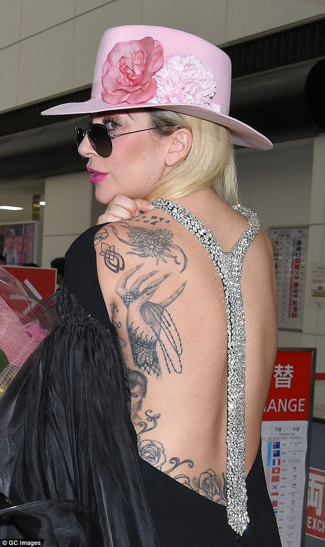 Artwork: Stepping through arrival with a big smile on her face, the 30-year-old Perfect Illusion singer cut a distinctive figure in a pink fedora and backless jumpsuit - flashing her tattoos