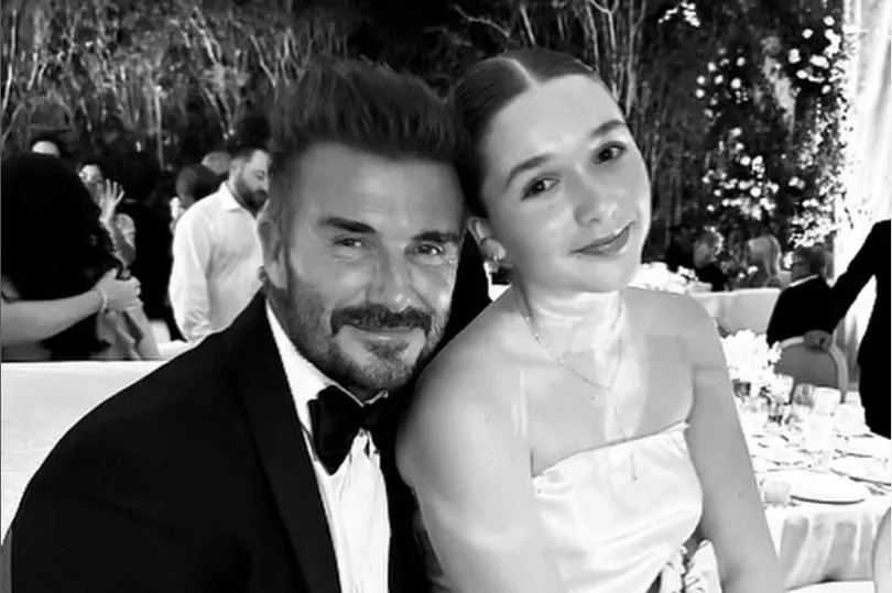 Black and white pic of David Beckham in a tux with daughter Harper on his knee