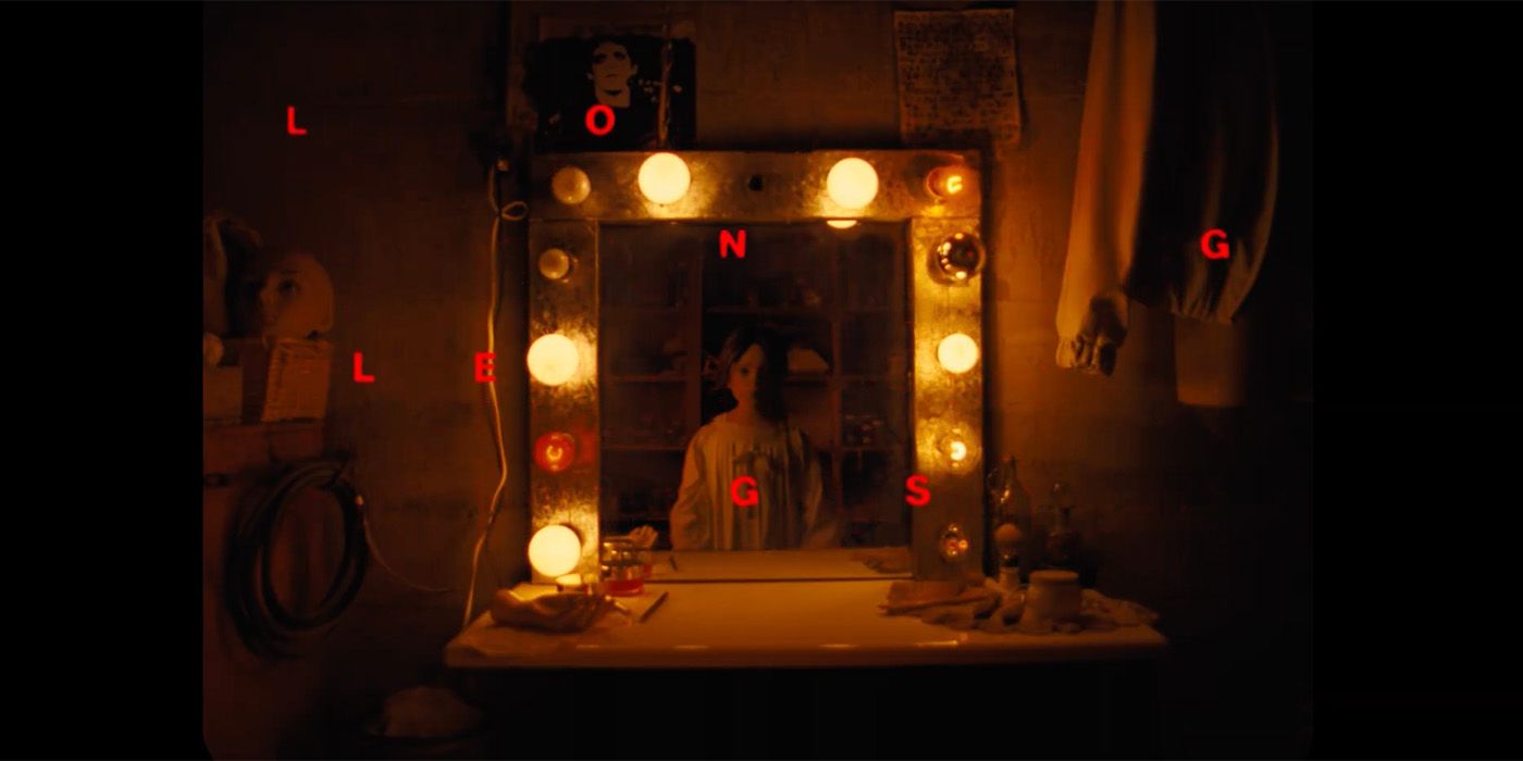 a little girl looking into a mirror with dim lights around it in horror movie Longlegs