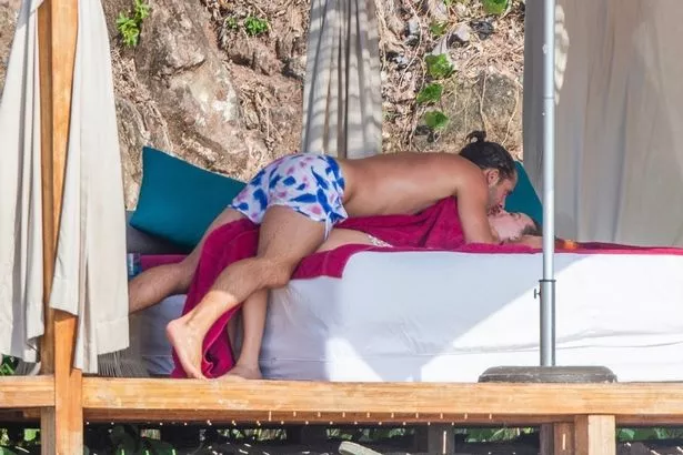 Tom tenderly plants a kiss on his wife during their beach outing