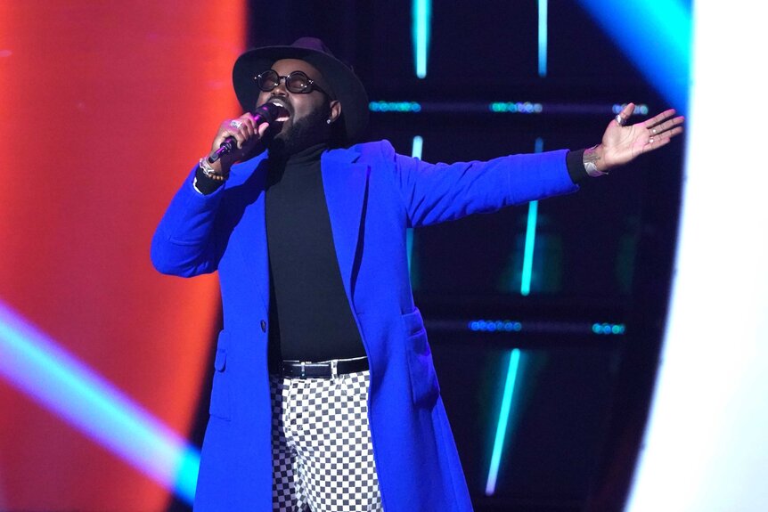 John Holiday wearing a blue coat singing on stage during the voice.